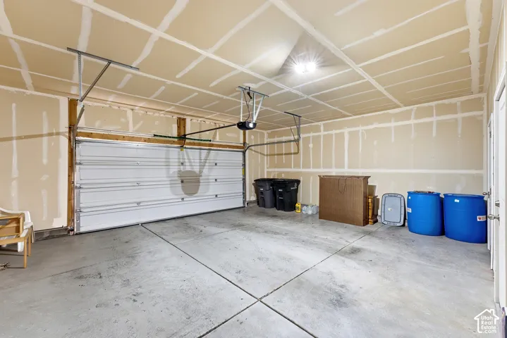 Concrete flooring, exposed stud walls, overhead lighting, garage door, and entry door