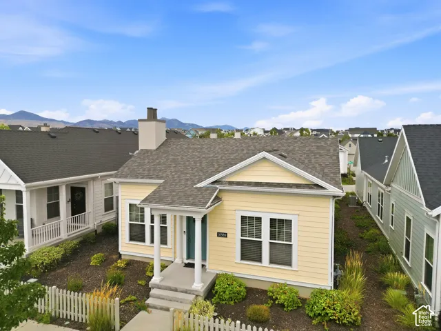 Yellow exterior siding, covered entryway, white picket fence, chimney structure, and dark shingle roof
