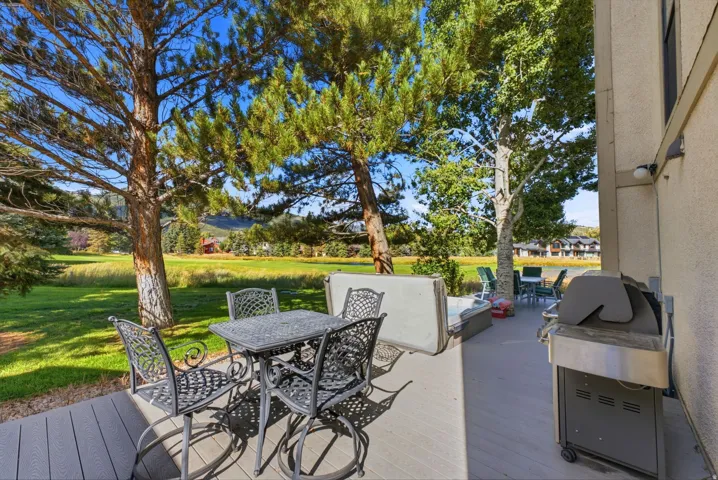 Expansive outdoor deck with a golf course backdrop, mature trees, and a spa