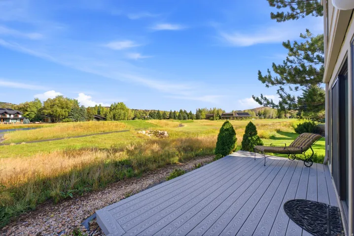 Spacious outdoor deck featuring composite decking, sliding glass door access, and expansive green space with mature trees