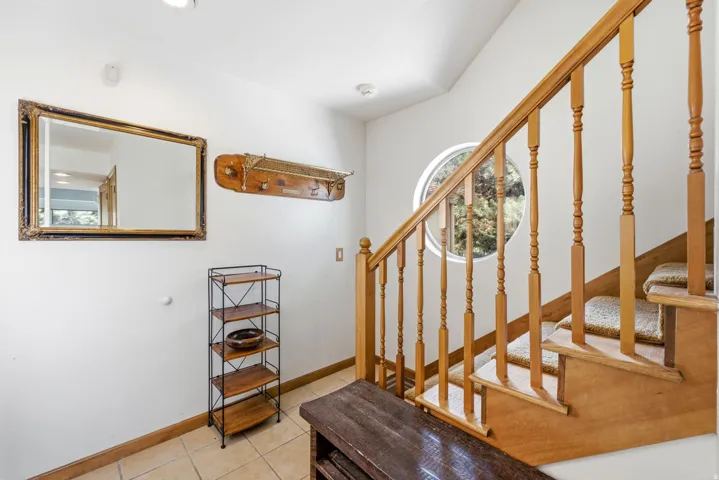 Hardwood staircase with baluster railing, round window, and tiled flooring
