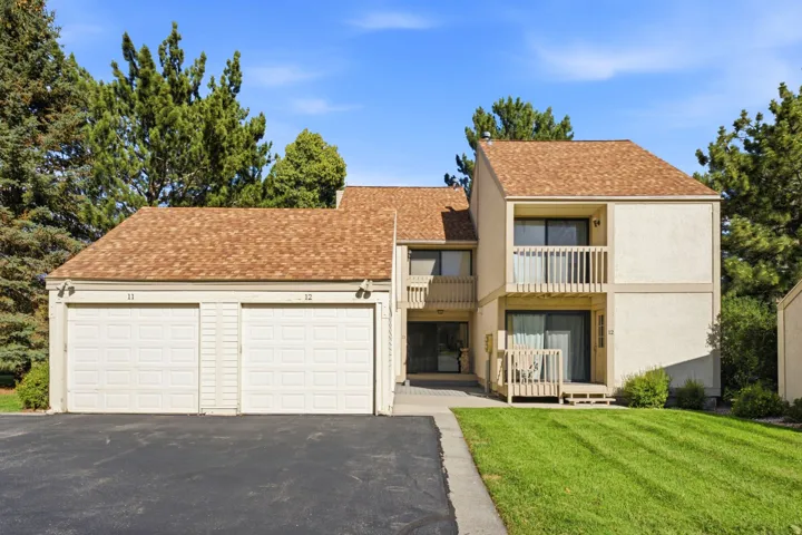 Exterior featuring a two-car garage, upper-level balcony, ground-level patio, and shingle roofing