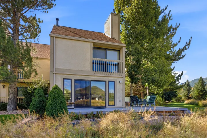 Two-story exterior with a stucco finish, featuring a second-level balcony, ground-level sliding glass doors, and an outdoor deck