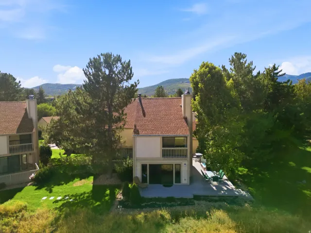 Multi-level dwelling with a neutral-toned exterior, an upper-level balcony, a ground-level patio, a shingle roof, and mature trees