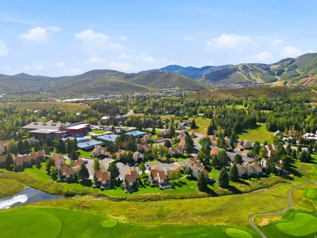 Green golf course, surrounding residential structures, natural water feature, and distant mountainous terrain