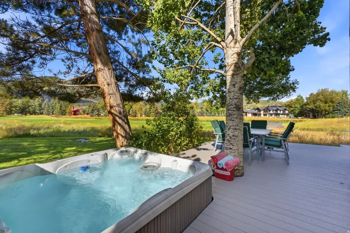 Expansive outdoor deck featuring a built-in hot tub, mature trees providing natural shade, and direct access to a grassy field
