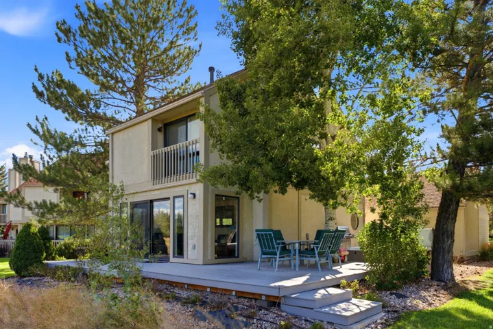 Multi-level exterior with a second-story balcony, ground-floor patio, and mature trees