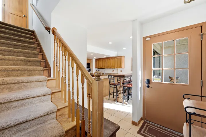 Carpeted staircase with wooden banister, tiled entry, and a kitchen featuring wood cabinetry