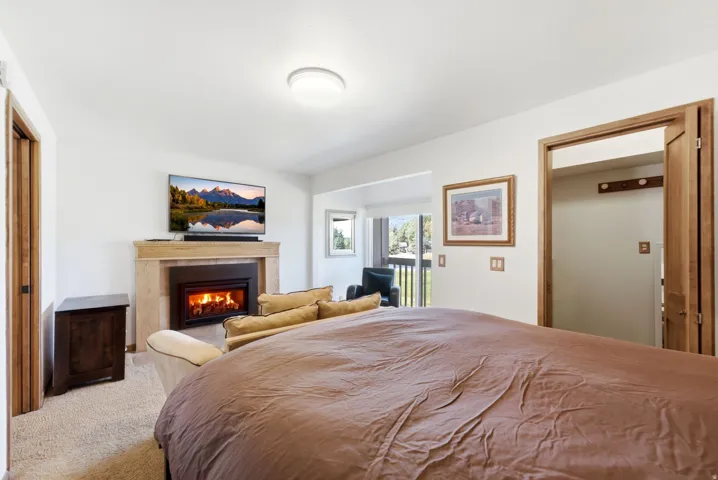 Gas fireplace with a stone surround, built-in shelving, carpet flooring, and a balcony