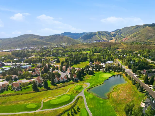 Expansive mountain landscape with surrounding ski slopes, a developed residential area, a golf course with greens, and a water feature