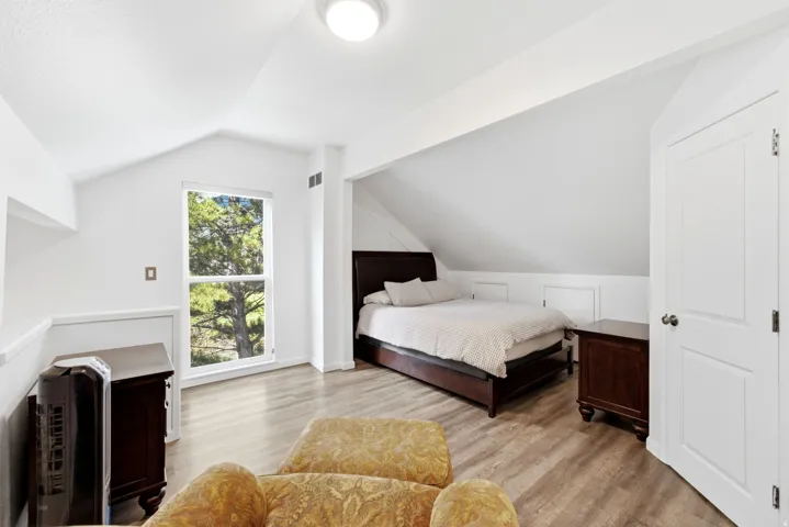 Vaulted ceiling, prominent window, wood-finish flooring, white paneled door, built-in storage panels