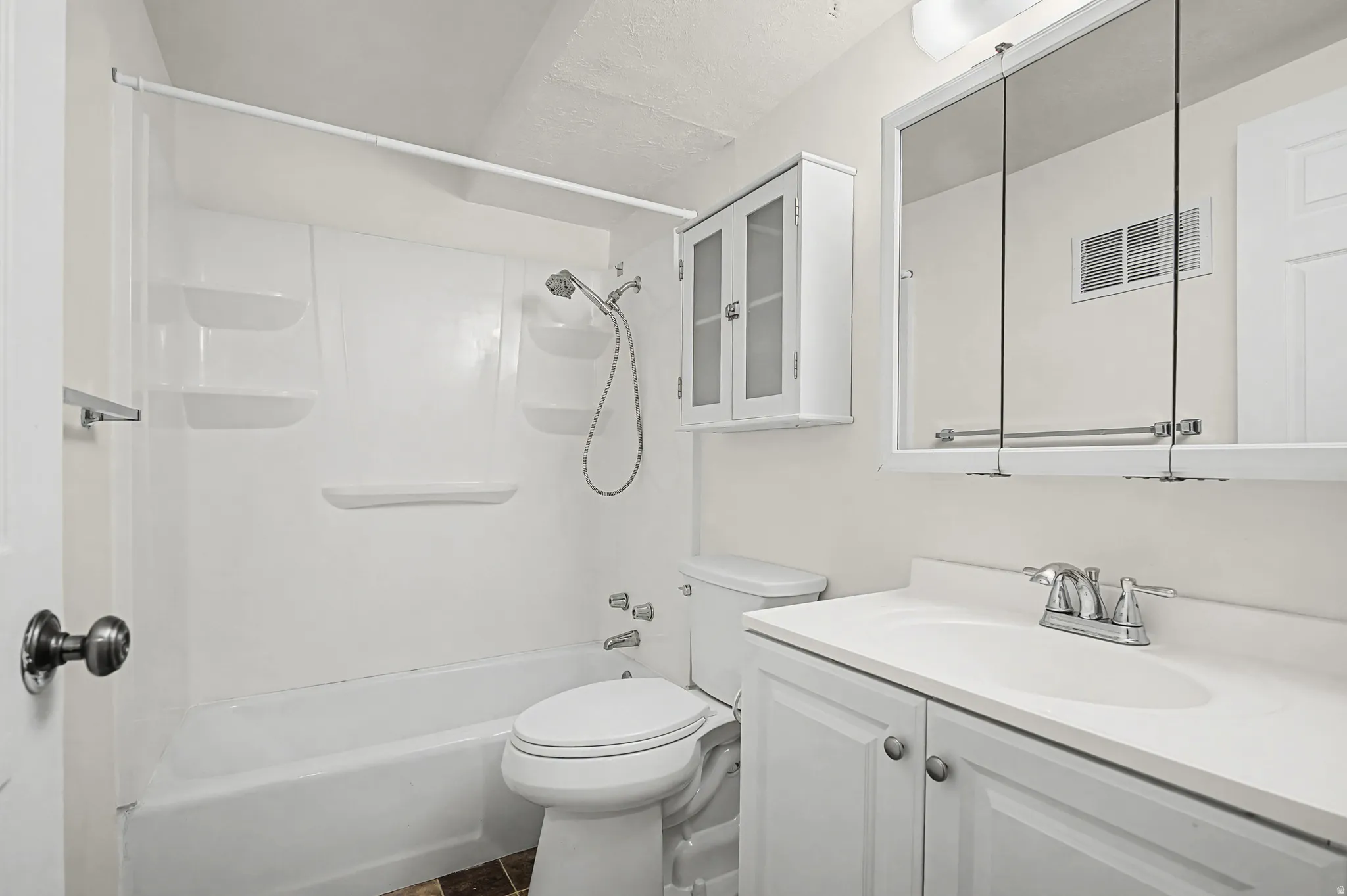 White vanity with a solid surface countertop, chrome faucet, mirrored medicine cabinet, and built-in wall cabinet with glass-front doors