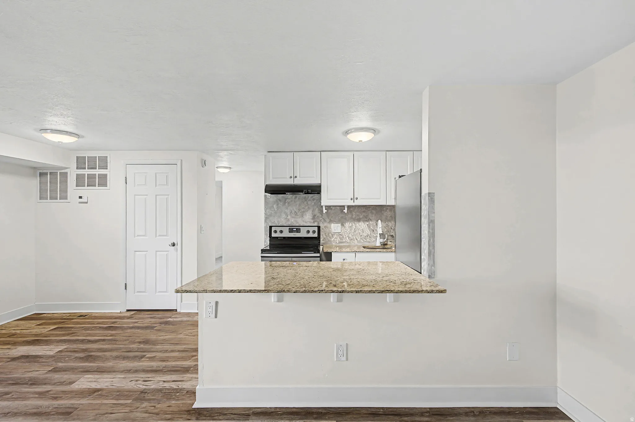Kitchen featuring white cabinetry, stone-finish backsplash, and stainless steel appliances