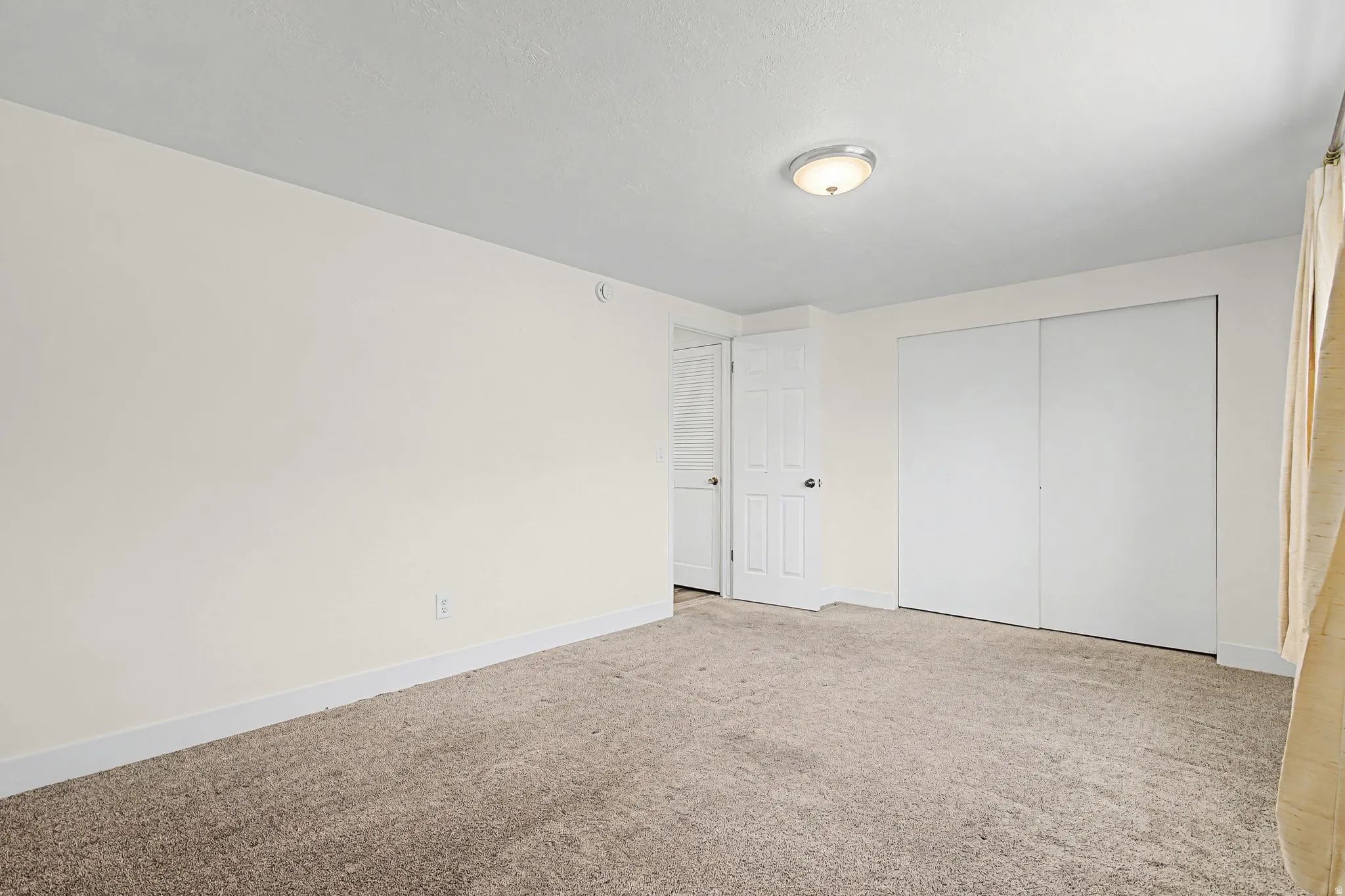 Carpeted flooring, white walls, white trim, overhead lighting, and white sliding closet doors
