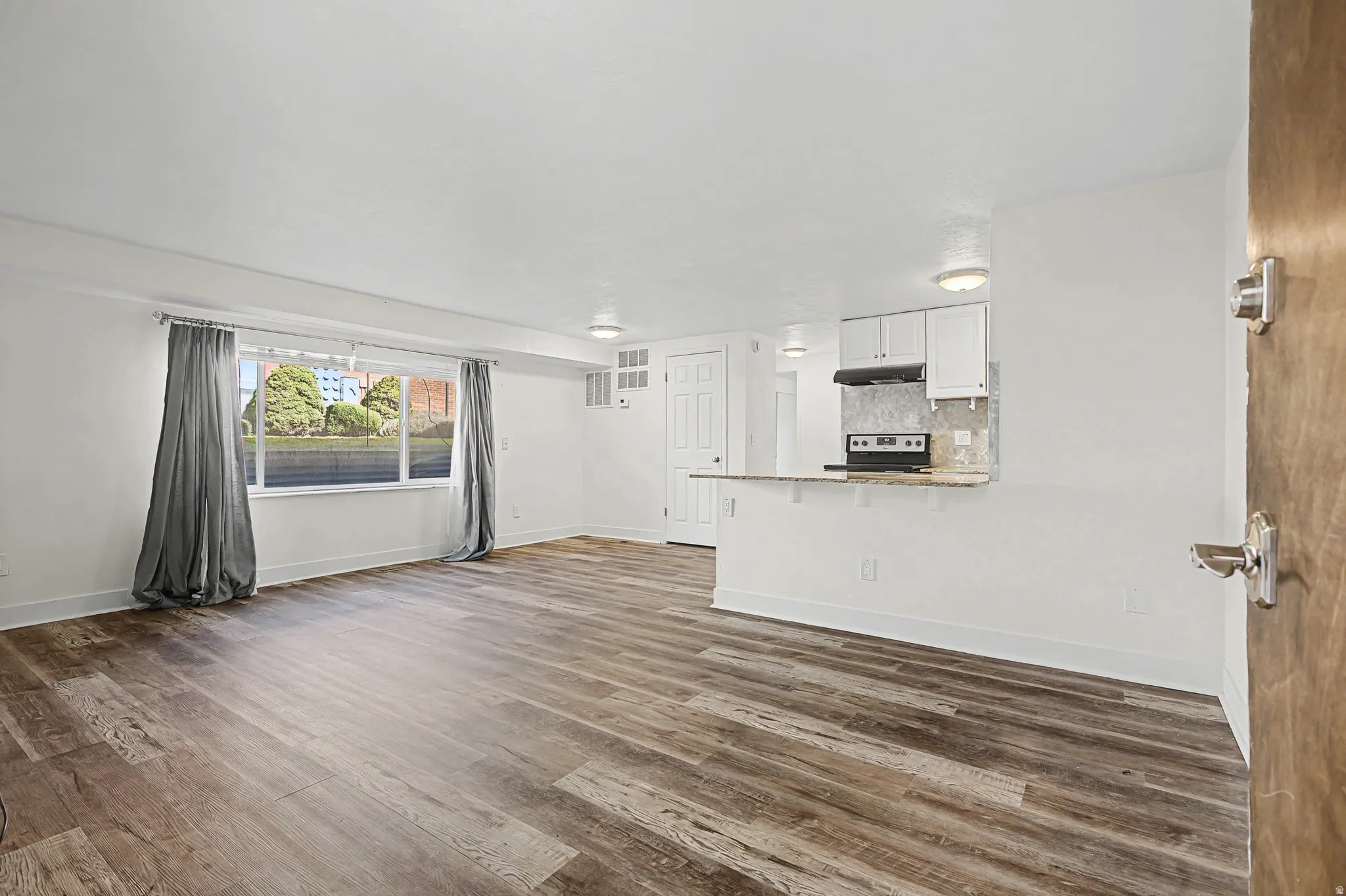 Wood-finish flooring, white cabinetry, integrated range, and a breakfast bar with stone-finish countertop