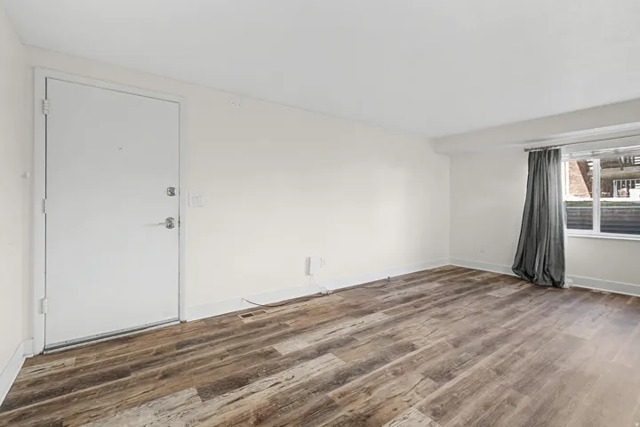 Wood-finish flooring with white baseboards, a white painted door, and a window with a fabric curtain