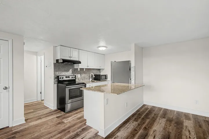 Updated kitchen featuring white cabinetry, stainless steel appliances, granite-look countertops, and wood-finish flooring