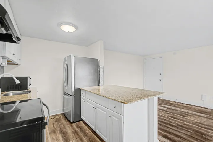 Kitchen featuring white cabinetry, stainless steel appliances, a kitchen island with a light-toned countertop, and wood-finish flooring