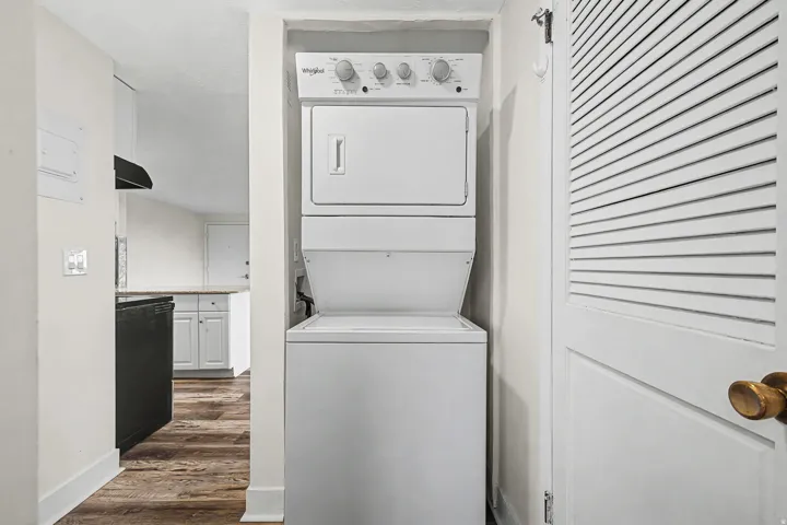 Stacked washer and dryer unit, wood-finish flooring, white cabinetry, light countertops, black range hood