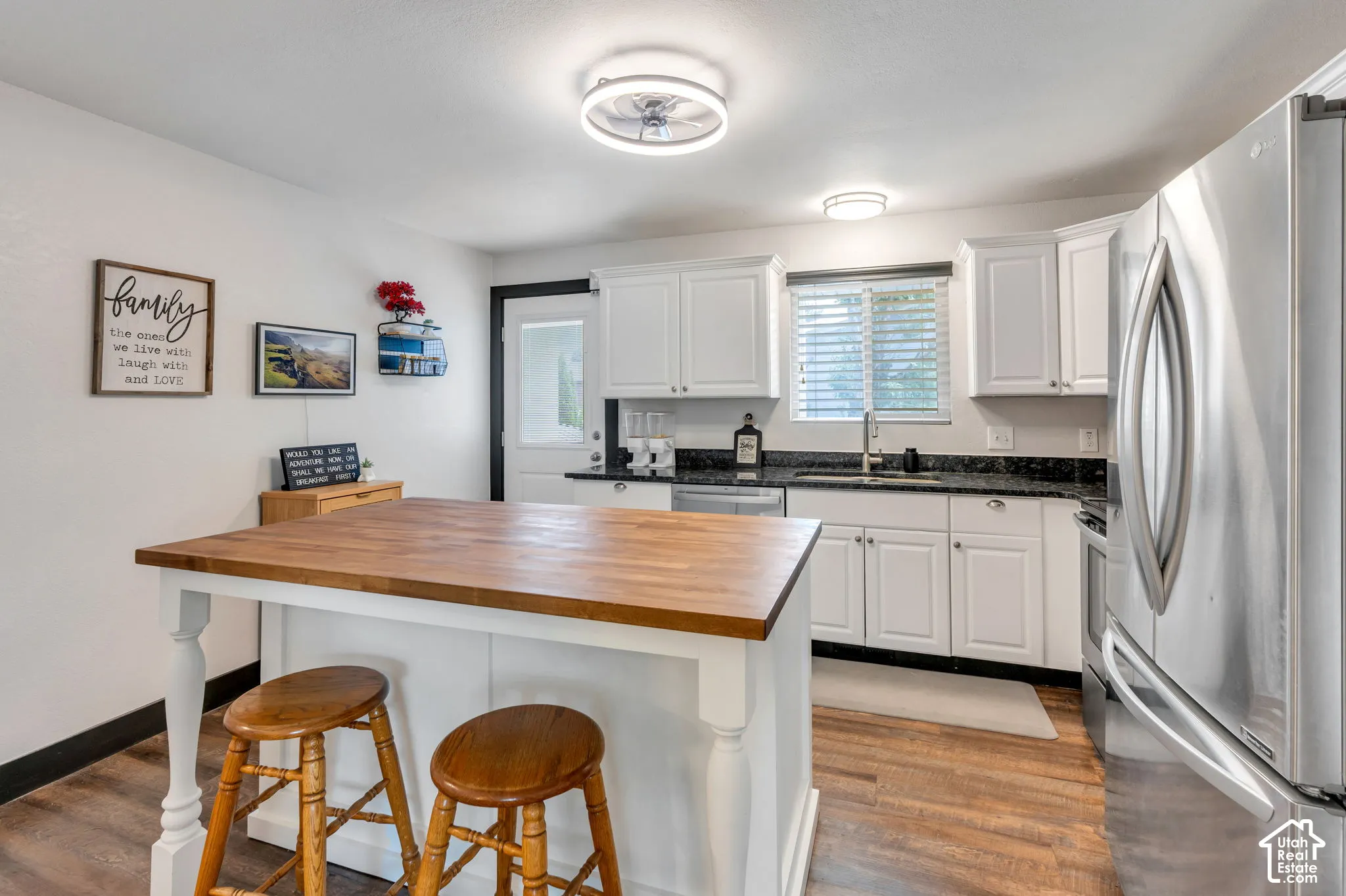 Kitchen featuring white cabinetry, dark countertops, wood-finish flooring, stainless steel refrigerator, and a built-in island with a wood countertop