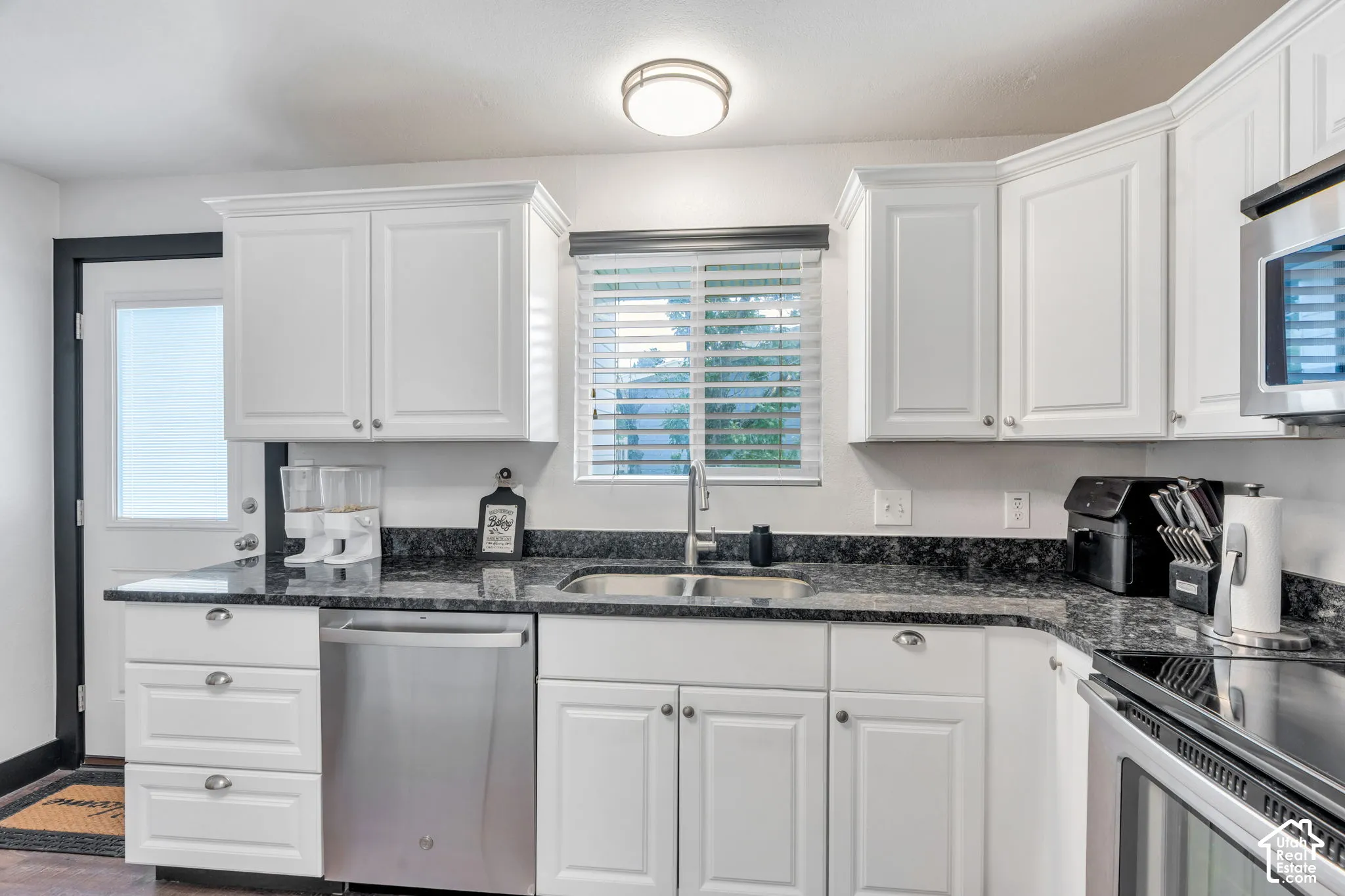 White cabinetry with crown molding, stainless steel appliances, dark stone countertops, undermount sink with a gooseneck faucet, and recessed lighting