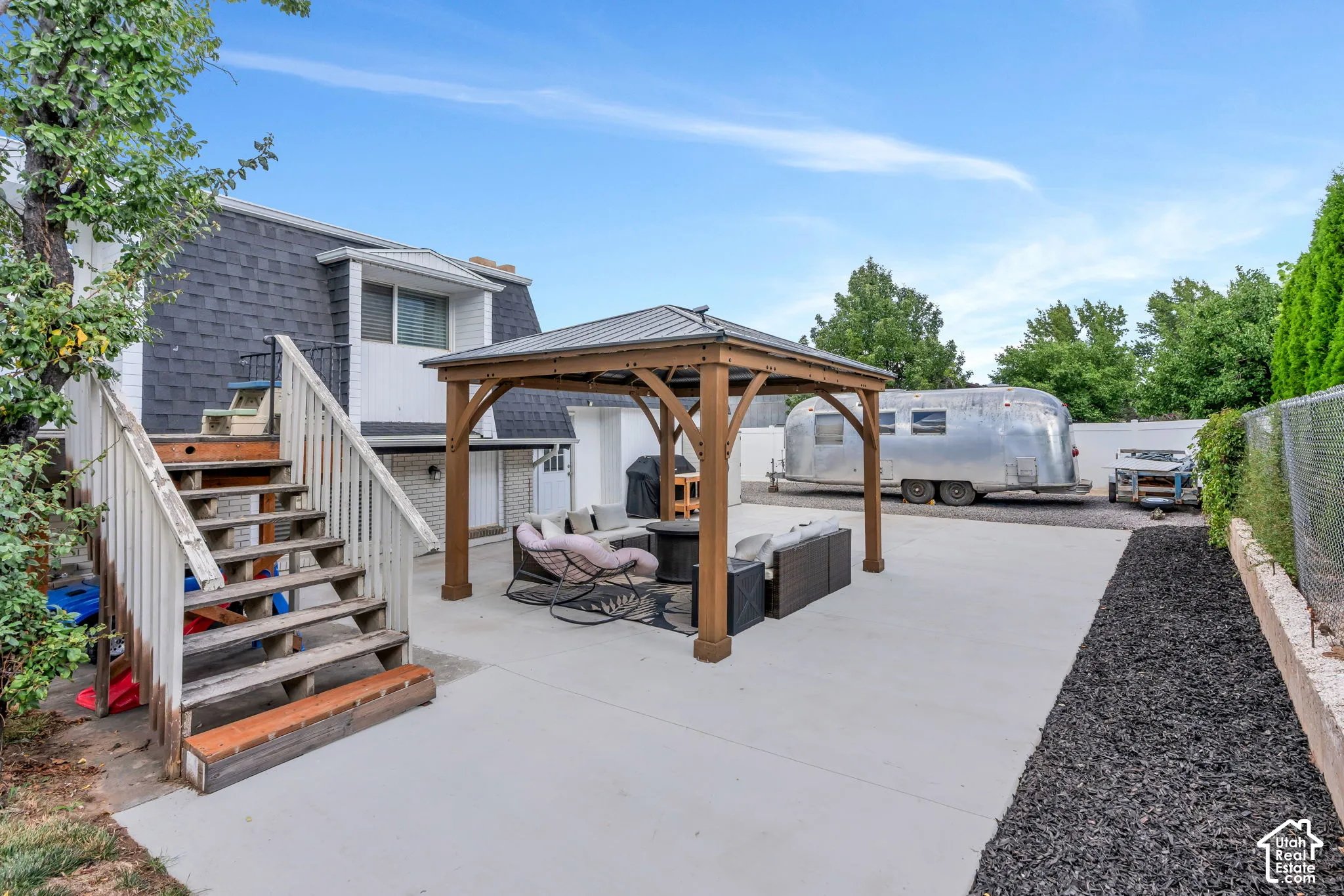 Spacious concrete patio with a permanent gazebo structure, stone accent landscaping, and a chain-link fence