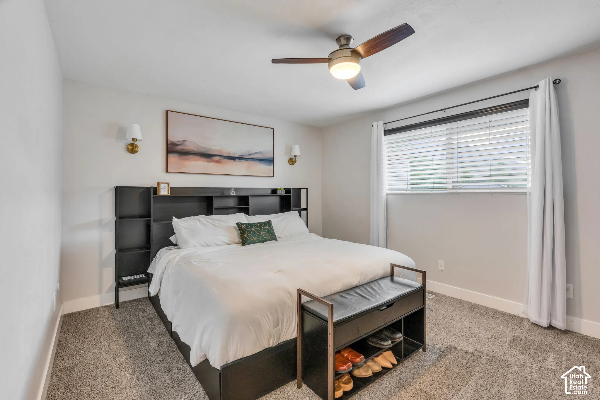 Plush carpet flooring, integrated shelving unit, modern ceiling fan with lighting, wall-mounted sconces, and window with blinds and drapes