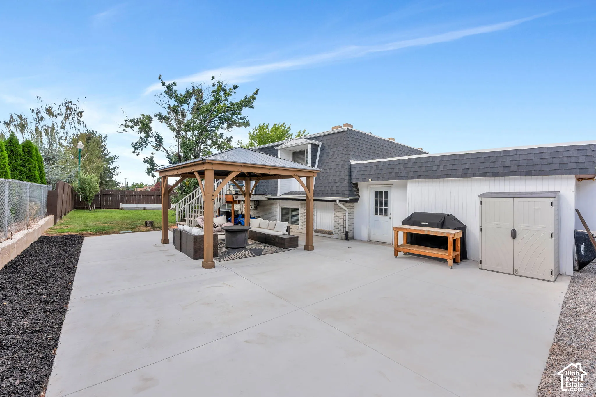 Expansive concrete patio with a permanent gazebo structure, adjacent to a manicured lawn area