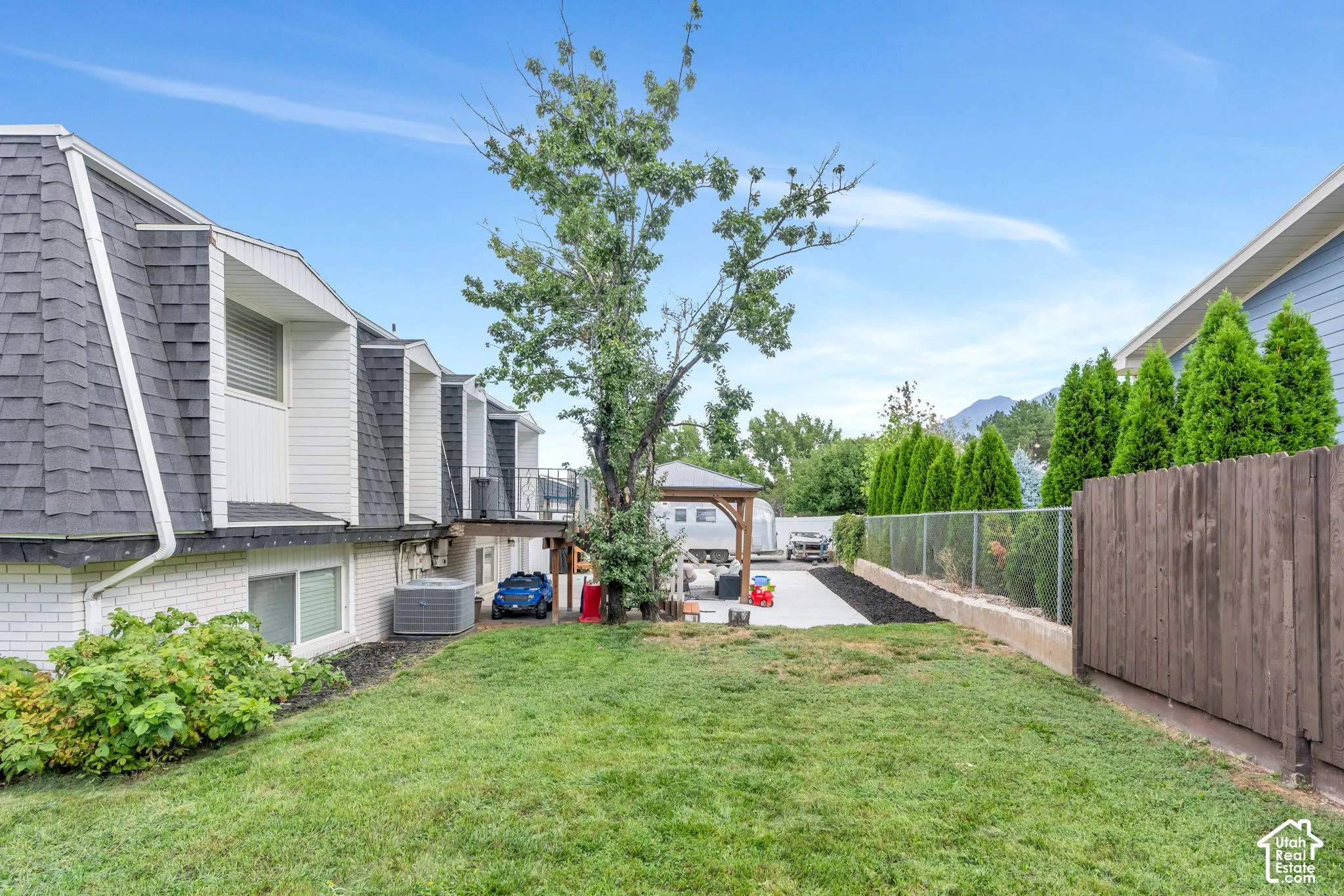 Expansive green lawn with a chain link fence, mature plantings, and a wooden privacy fence