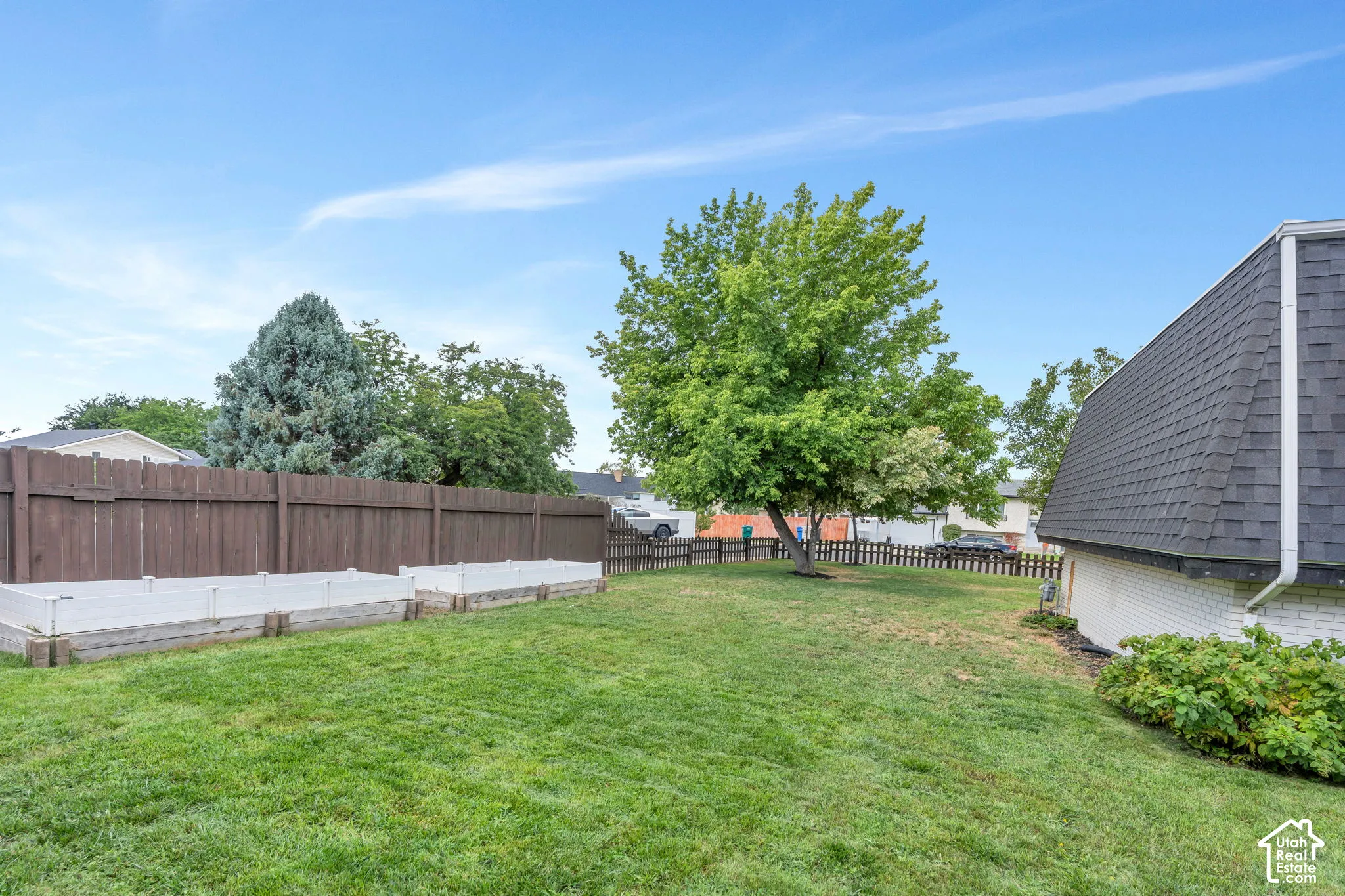 Expansive backyard featuring a lush lawn, two raised garden beds, a wood privacy fence, and mature trees