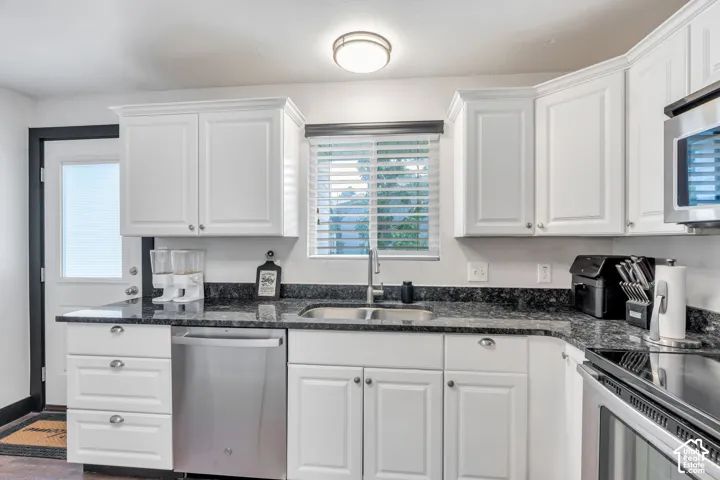 White cabinetry with crown molding, stainless steel appliances, dark stone countertops, undermount sink with a gooseneck faucet, and recessed lighting