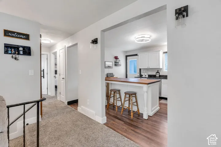 Kitchen island with wood-finish countertop, white cabinetry, dark countertops, and wood-finish flooring