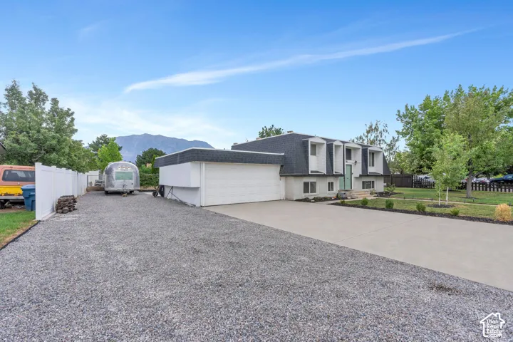 Property exterior featuring a gravel driveway, concrete driveway, attached garage, and mature trees
