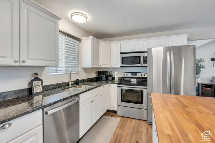 Kitchen featuring white cabinetry, dark stone countertops, stainless steel appliances, and wood-finish flooring