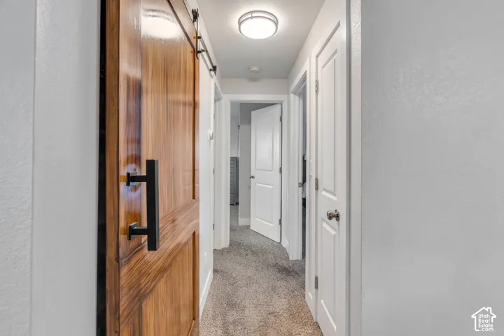Hallway featuring a wood-finish barn door with a matte black handle, neutral carpeting, and recessed lighting