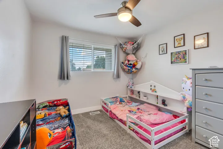 Carpeted flooring with a window, ceiling fan, and white walls