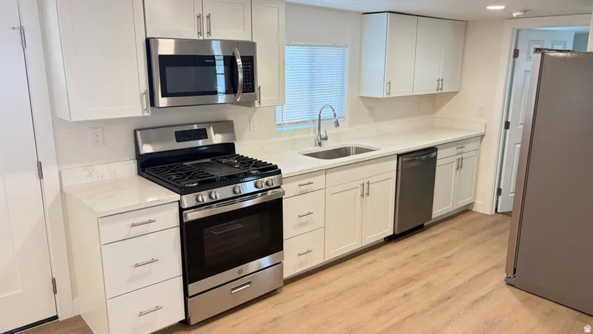 White shaker-style cabinetry, stainless steel appliances, light-toned wood-finish flooring, white countertops, and a stainless steel sink