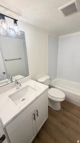Bathroom featuring a white vanity with an integrated sink and light-colored countertop, chrome faucet, wood-finish flooring, and a white bathtub with a shower surround