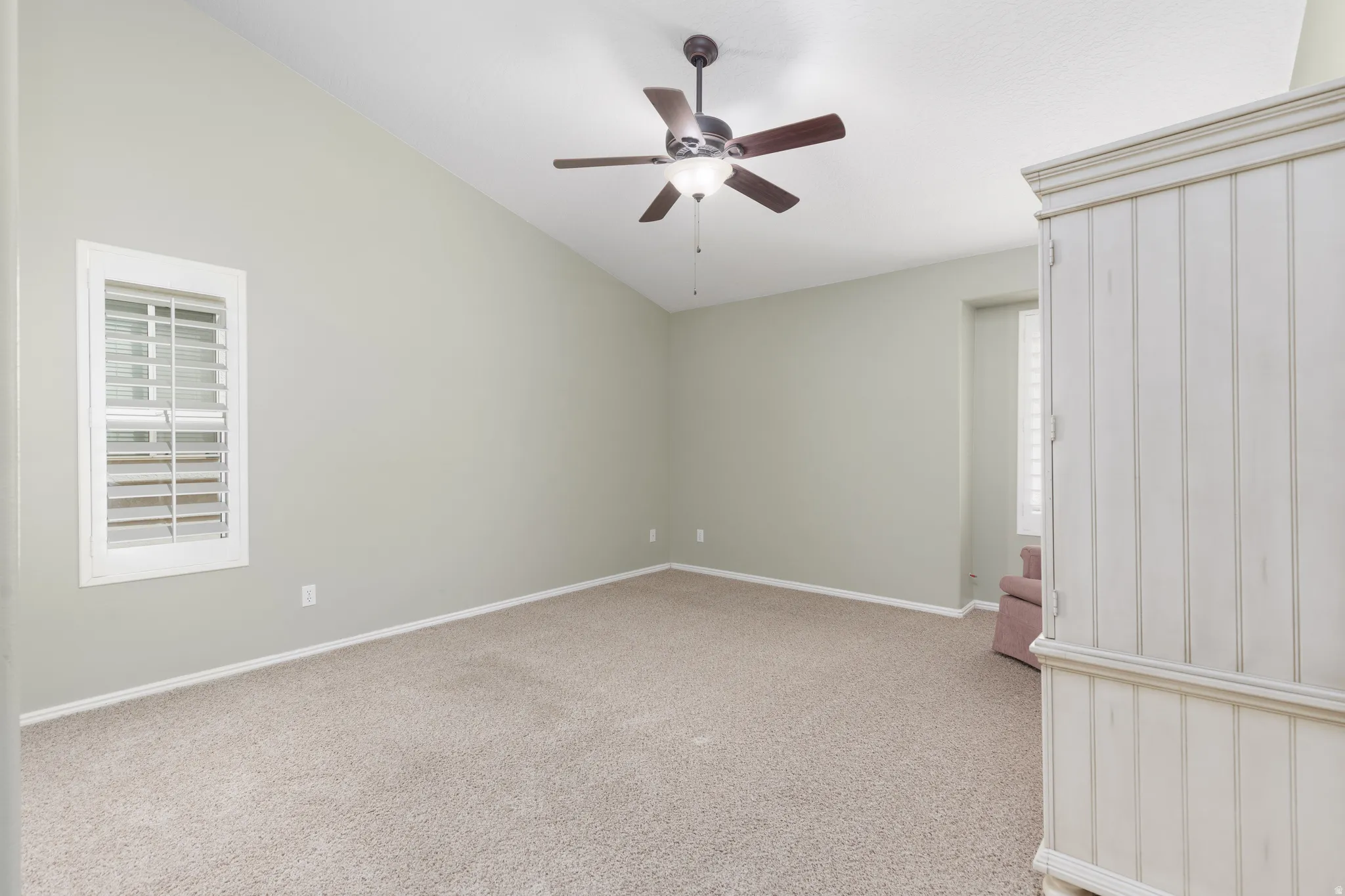 Vaulted ceiling with a ceiling fan, window with plantation shutters, and carpeted flooring