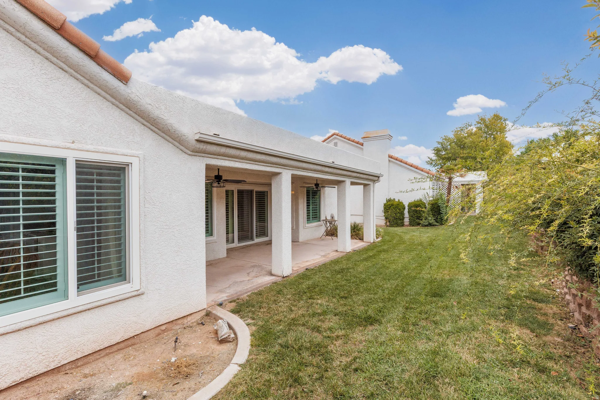Expansive backyard featuring a covered patio, stucco exterior, multiple windows with shutters, and a well-maintained lawn