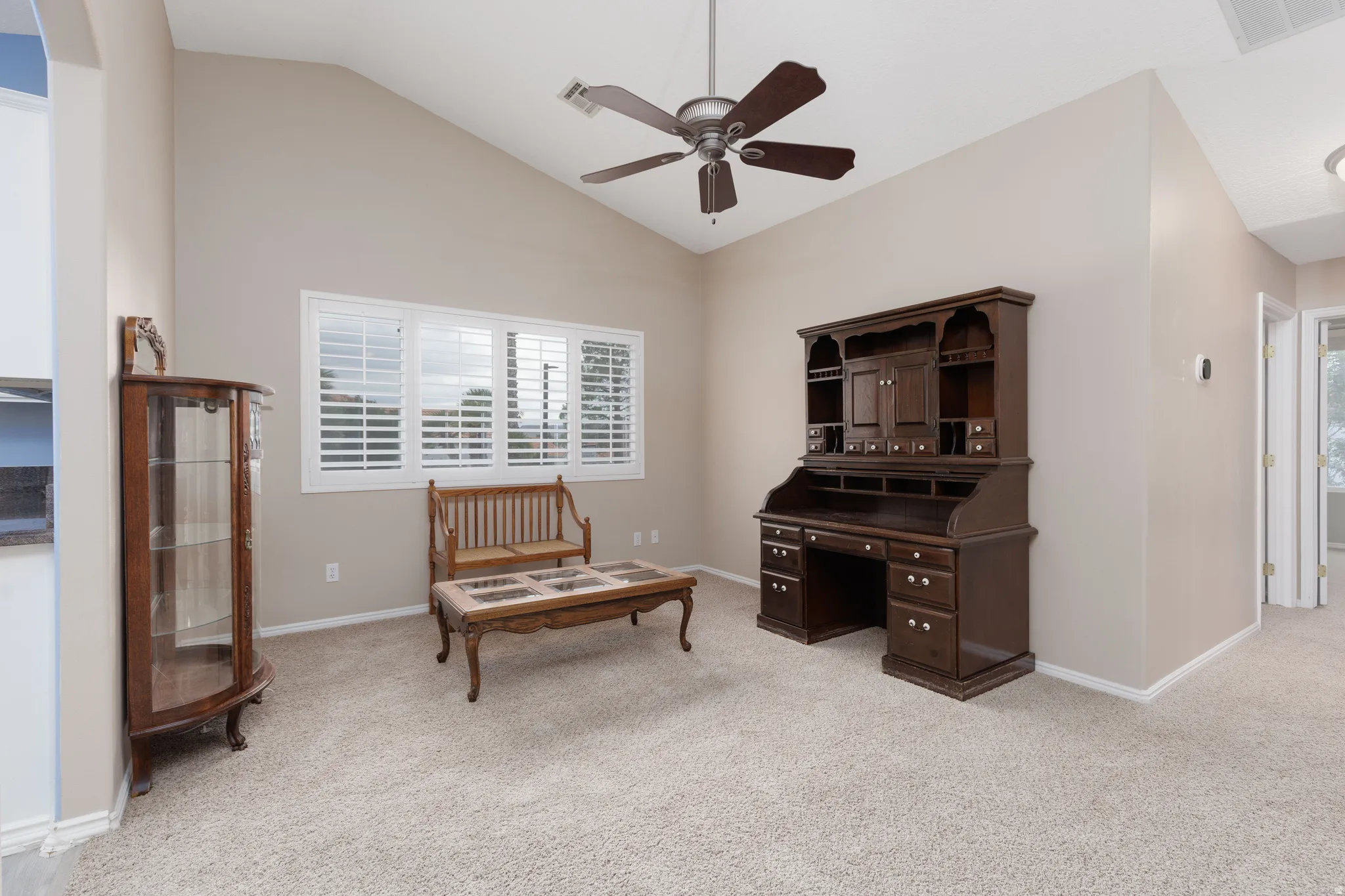Vaulted ceiling with a ceiling fan, white window shutters, and neutral-toned carpeting