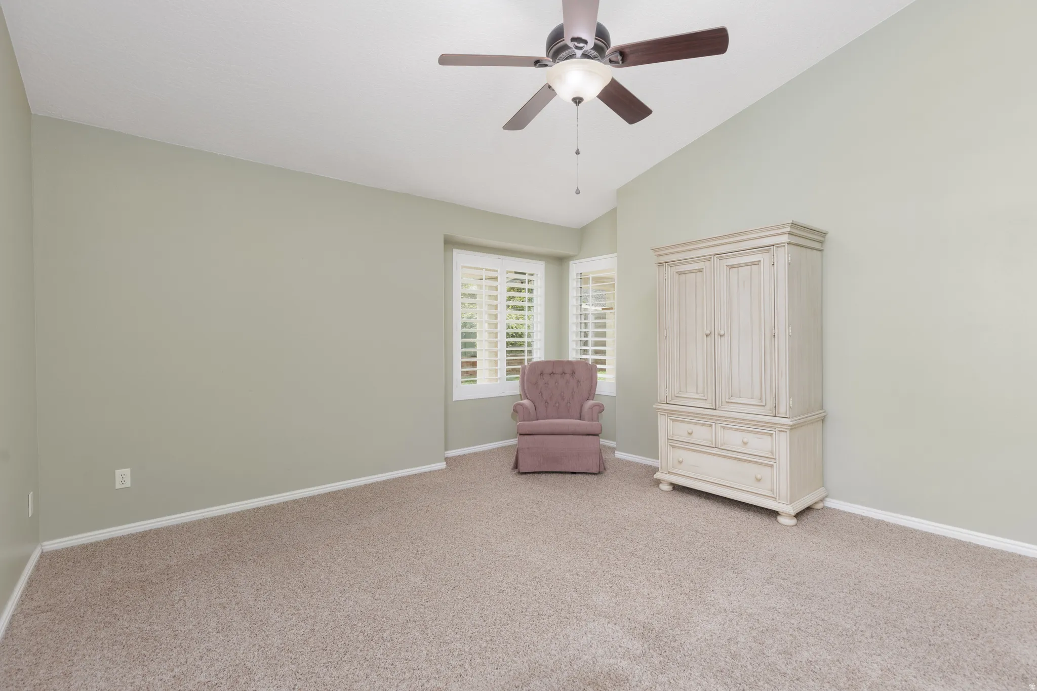 Vaulted ceiling with a ceiling fan, bay window with plantation shutters, and carpeted flooring