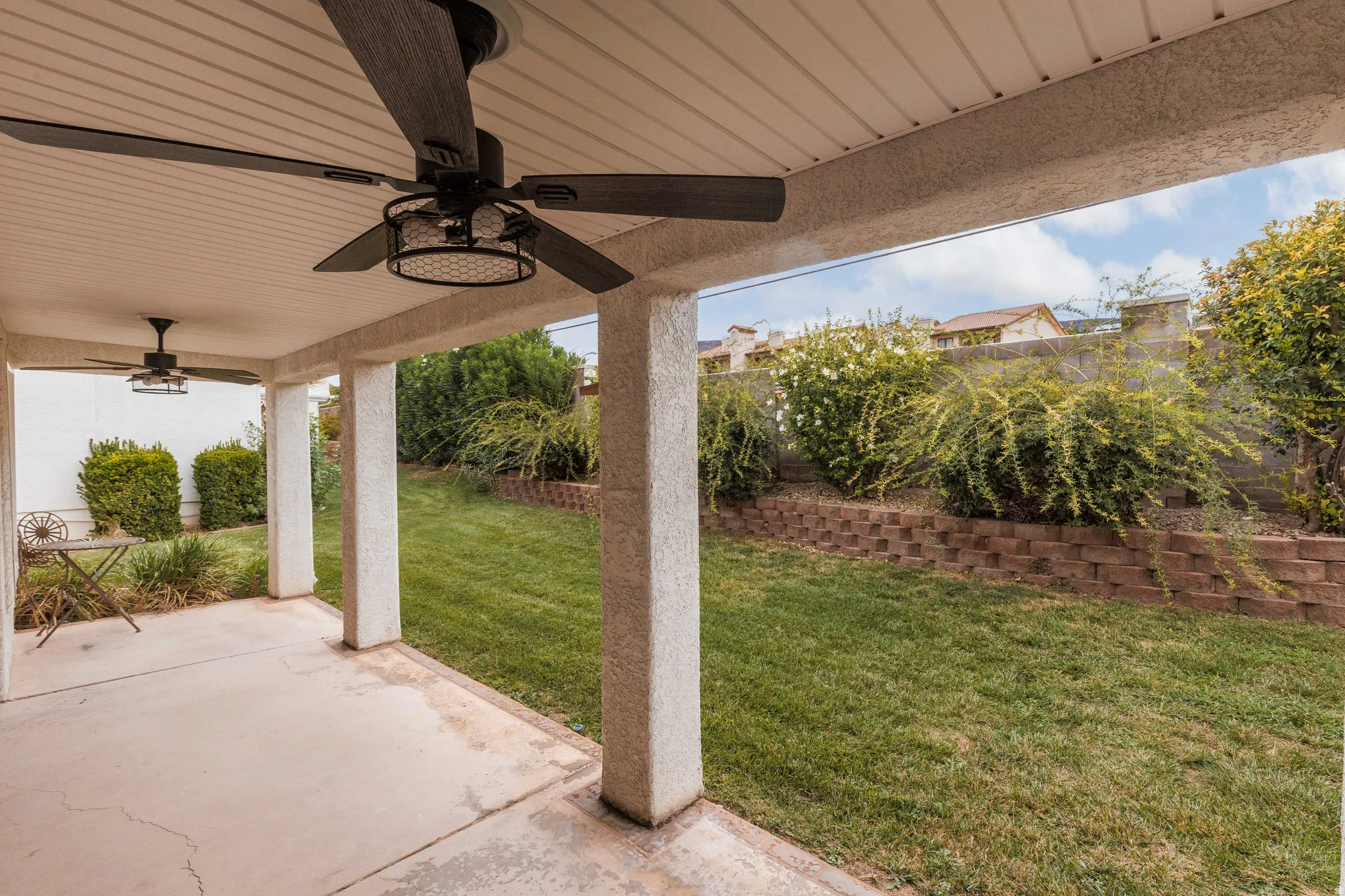 Covered patio with dual ceiling fans, concrete flooring, and support columns