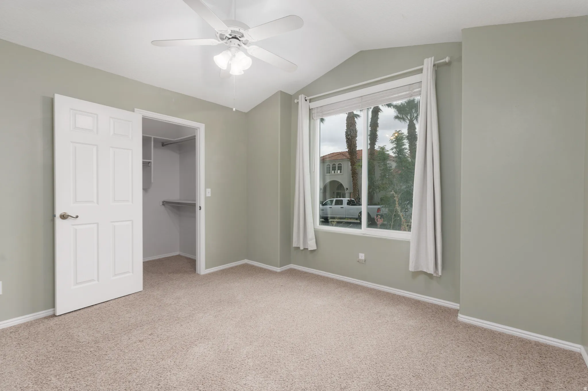 Vaulted ceiling featuring a ceiling fan, carpet flooring, a window with curtains, and a built-in closet with shelving
