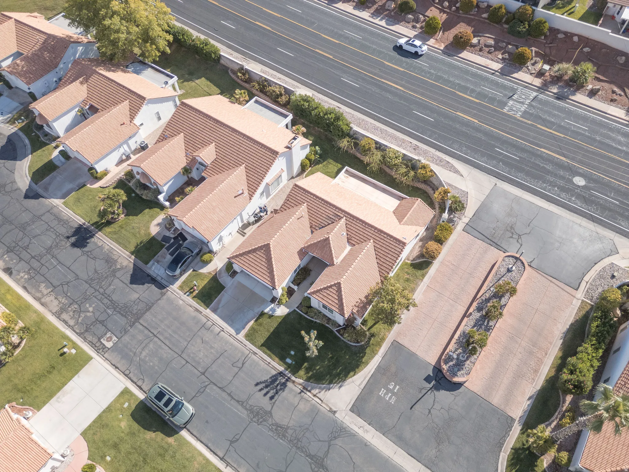 Residential property with terracotta-tiled roofs, a paved driveway, and established landscaping