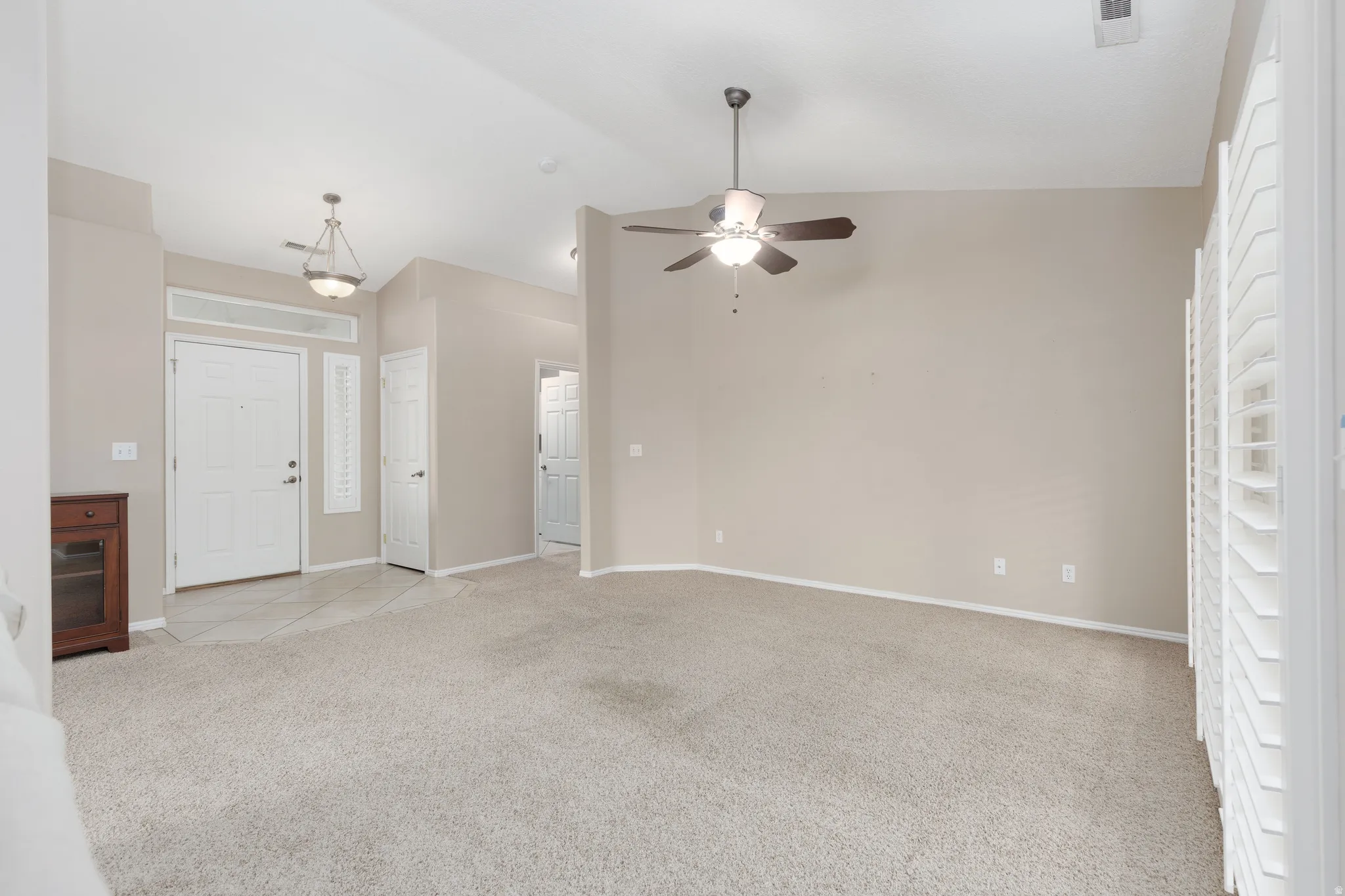 Vaulted ceiling, ceiling fan, white paneled doors, shuttered windows, and neutral carpeting