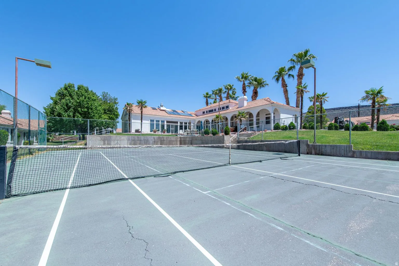 Outdoor tennis court with a net, bordered by fencing and concrete retaining walls