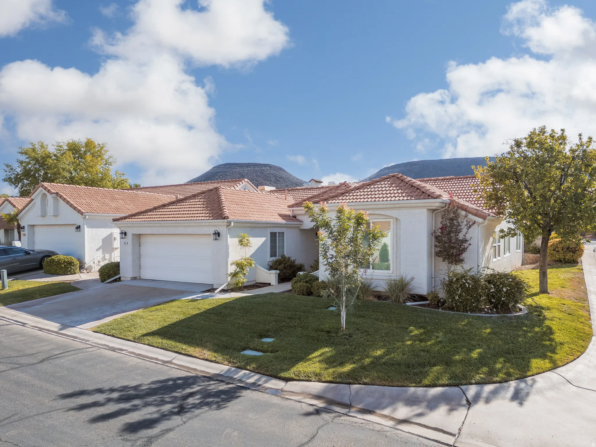 White stucco exterior with a tile roof, featuring an attached garage and a manicured lawn