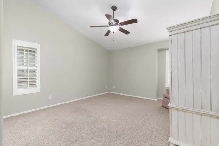 Vaulted ceiling with a ceiling fan, window with plantation shutters, and carpeted flooring