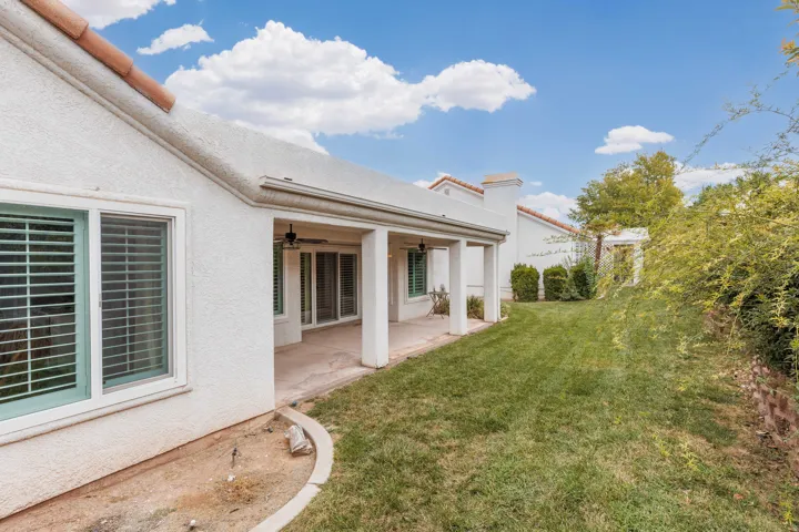 Expansive backyard featuring a covered patio, stucco exterior, multiple windows with shutters, and a well-maintained lawn